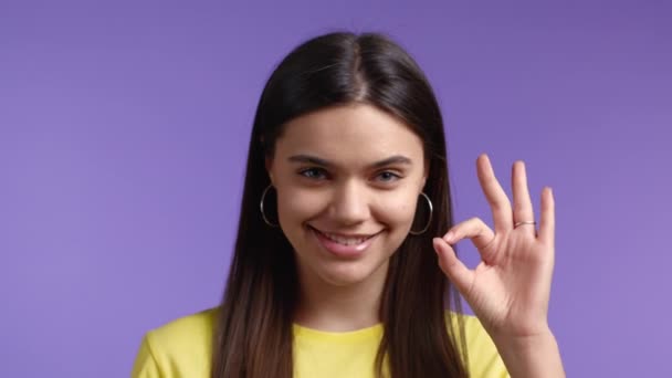 Женщина крупным планом показывает знак ОК на фоне фиолетовой студии. Позитивная молодая девушка улыбается в камеру. Победитель. Успех. Язык тела. — стоковое видео
