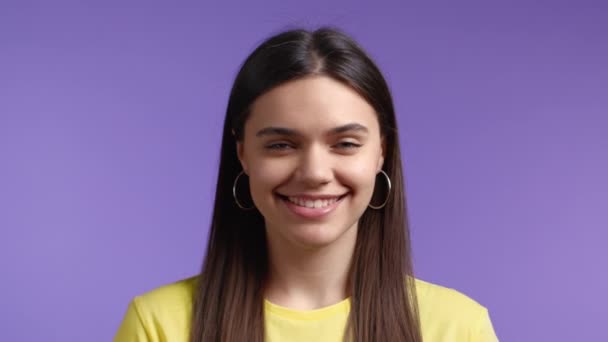 若いクローズアップ女性の長い髪のカメラを探して、笑みを浮かべて。美しいですモデル女の子で黄色tシャツ上の紫のスタジオの背景. — ストック動画