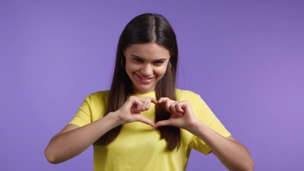 Mulher bonita gentil fazendo sinal de forma coração perto de seu peito. Fundo violeta. Saúde da mulher, voluntariado, ajuda de doação e conceito de amor. — Vídeo de Stock