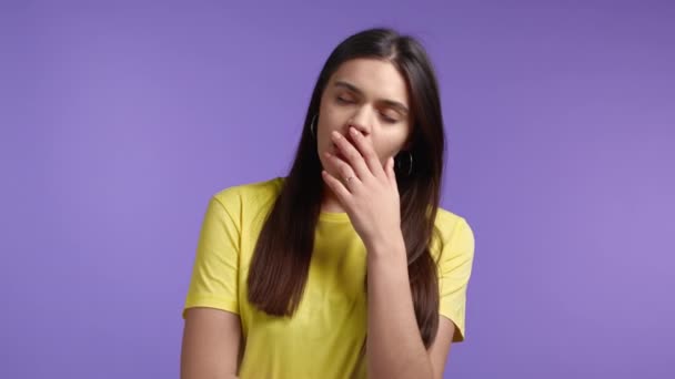 Tired sleepy woman yawns, covers her mouth with hand. Girl stretches hands up. Very boring, uninteresting. Violet studio background. — Stock Video