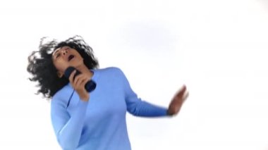 Kablosuz taşınabilir hoparlörden müzik dinleyen Afrikalı bir kadın. Modern ses sistemi. Genç kız dans ediyor, beyaz stüdyo geçmişiyle eğleniyor. Müziğin ritmine göre hareket eder..