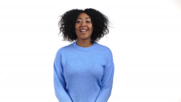Donna africana con i capelli ricci guardando la macchina fotografica, sorridente. Bella ragazza modello in maglione blu su sfondo bianco studio. — Video Stock
