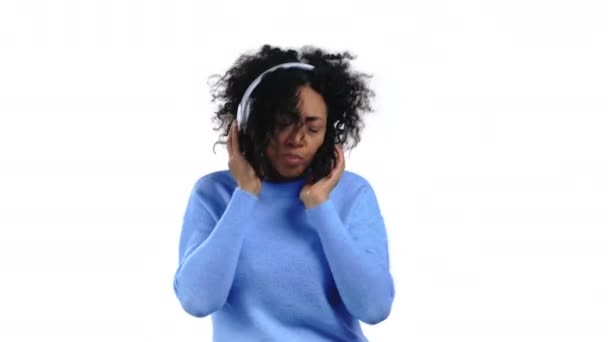 Mujer bastante africana bailando con auriculares inalámbricos aislados en el fondo del estudio blanco. Retrato de chicas lindas. Música, radio, felicidad, libertad, concepto de juventud. — Vídeos de Stock