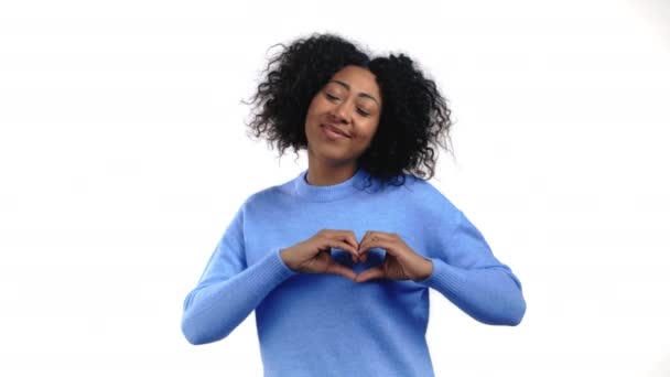 Mujer africana amable haciendo señal de forma corazón cerca de su pecho. Fondo blanco. Salud de las mujeres, voluntariado, ayuda para la donación y concepto de amor. — Vídeo de stock