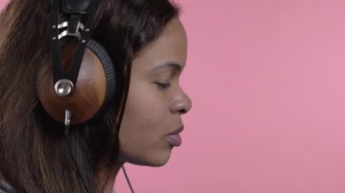 Pembe stüdyo arka planında kulaklıkla dans eden Afrikalı kadın. Hoş bir bayan portresi. Müzik, radyo, mutluluk, özgürlük, gençlik kavramı.