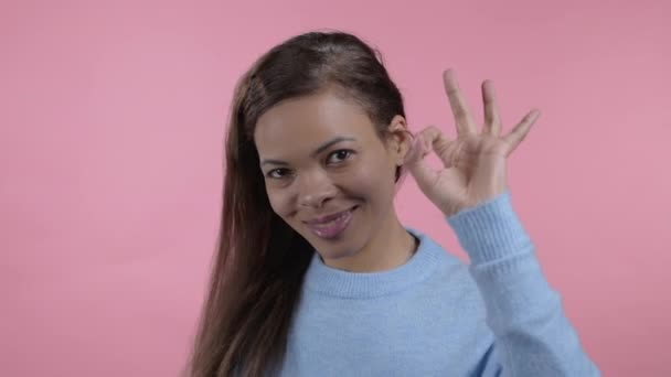 Mujer africana mostrando Ok signo sobre fondo de estudio rosa. Chica joven y positiva sonríe a la cámara. Ganador. Éxito. Lenguaje corporal. — Vídeo de stock