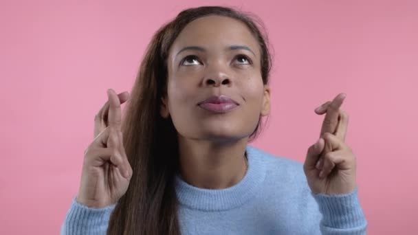 Afrikai nő imádkozik keresztbe tett ujjakkal rózsaszín háttér. A lány könyörög valakinek, hogy elégítse ki a vágyait, segítsen neki.. — Stock videók