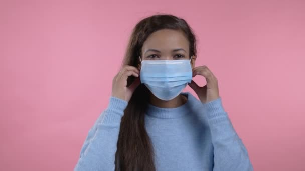 Pleased african woman removed protective mask and throws it on floor as symbol of pandemic, epidemic end. Pink studio background. — Stock Video