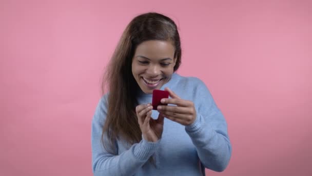 Mulher africana segurando pequena caixa de jóias com anel de diamante proposta no fundo da parede rosa. Senhora sorrindo, ela está feliz por estar presente, proposta de casamento — Vídeo de Stock