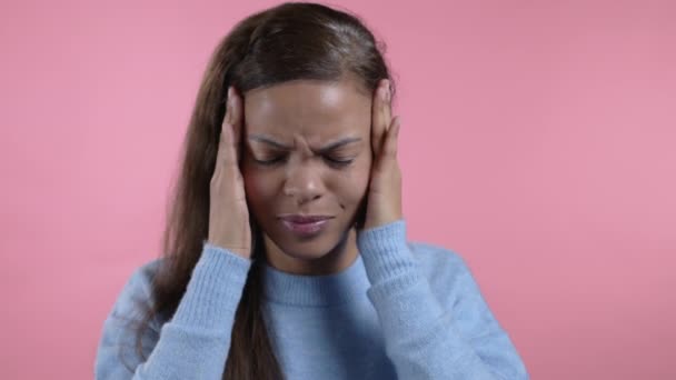 Portret van een Afrikaanse vrouw met hoofdpijn, roze atelierportret. Meisje met handen op het hoofd. Concept van migraine problemen, geneeskunde, ziekte — Stockvideo