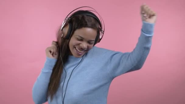 Vegyes rasszista nő táncol vicces fülhallgató elszigetelt rózsaszín stúdió háttér. Aranyos hölgy. Zene, rádió, boldogság, szabadság, ifjúságpolitika. — Stock videók