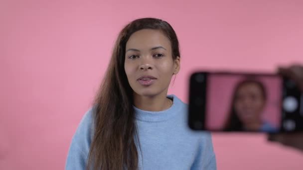 온라인으로 새로운 비디오 블로그 인 vlog 를 만들고 있는 아프리카 블로거 여성 이 분홍색 배경에 스마트폰을 가지고 있습니다. 콘퍼런스 콜 레코드중 카메라로 통화하는 영향. — 비디오