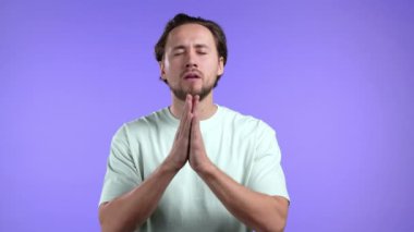 Klasik tişörtlü genç adam menekşe arkaplanı için dua ediyor. Adam birine arzularını tatmin etmesi için yalvarıyor..