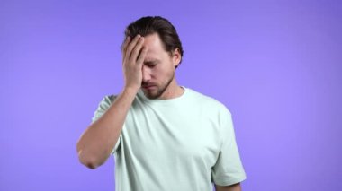 Sıkılmış üzgün adam menekşe arka planda iç çeker. Hoşnutsuzluk içindeki yakışıklı adam, durumdan bıkmış, kendini iyi hissetmiyor. 4k