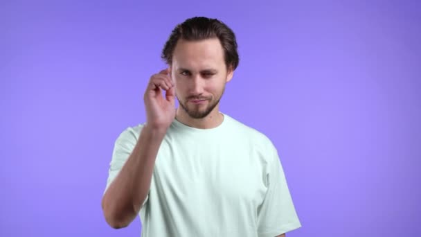 Charmant homme pointe index dans l'objectif de la caméra et clins d'oeil, flirts. Hé, toi Guy en t-shirt basique sur fond violet. — Video