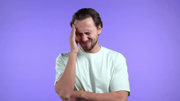 Young man having headache, studio portrait. Guy putting hands on head, isolated on violet background. Concept of problems, medicine, illness — Stock Video