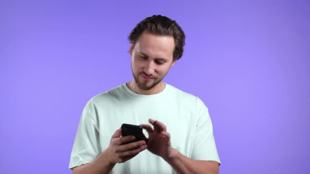 Violet stüdyo duvarında akıllı telefon kullanan yakışıklı bir adam. Modern teknolojiyi kullanarak - uygulamalar, sosyal ağlar. — Stok video