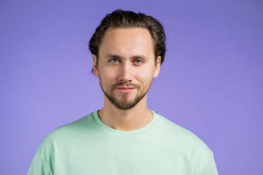 Kameraya bakan neşeli Avrupalı adamın portresi. Stüdyoda mor arka planda gülümseyen yakışıklı genç adam..