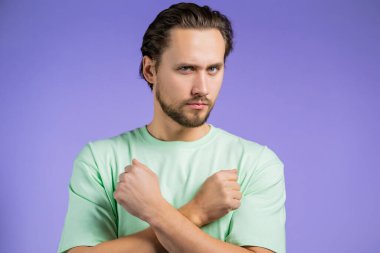 Eli çapraz olmayan ciddi bir adamın portresi Basta 'yı, olumsuzluğu, yeterli jesti yapar. İnkar etmek, reddetmek, anlaşmazlık. Mor arka planda yakışıklı bir adamın portresi.