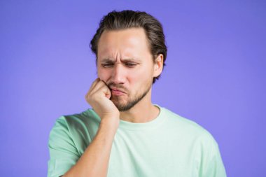 Violet stüdyosunun arka planında diş ağrısı olan yakışıklı bir genç. Diş ağrısı, diş sorunları, stomatoloji ve tıp konsepti.