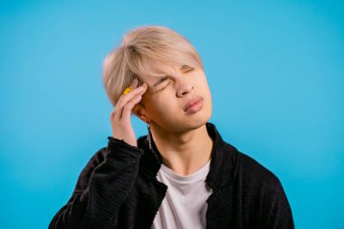 Asyalı adam baş ağrısı çekiyor, stüdyo resmi. Koreli stil sahibi adam ellerini başının üstüne koyuyor, mavi arka planda izole edilmiş. Sorunlar, ilaç, hastalık kavramı