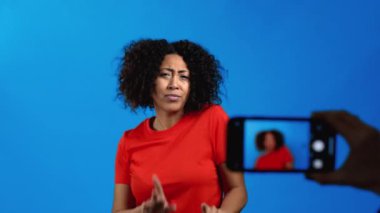 Gülümseyen Afrikalı kadın mavi arka planda akıllı telefon kamerasının önünde dans ederken videosunu kaydediyor. Nüfuz Edici komik sosyal medya klibi yapıyor