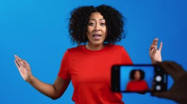 Gülümseyen Afrikalı blogcu kadın çevrimiçi yeni bir video blogu yapıyor, mavi arka planda akıllı telefonu olan bir video blogu. Konferans kayıtları sırasında kameraya konuşan nüfuzlu kişi.