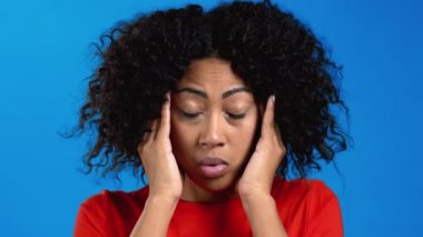 Baş ağrısı çeken Afrikalı bir kadının portresi, mavi stüdyo resmi. Ellerini başının üstüne koyan bir kız. Migren sorunları, ilaç, hastalık kavramı