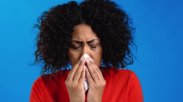 Afrikansk kvinna nyser i vävnad. Isolerad flicka på blå studio bakgrund. Damen är sjuk, har en förkylning eller allergisk reaktion. Coronavirus, epidemi 2021, sjukdomskoncept — Stockvideo