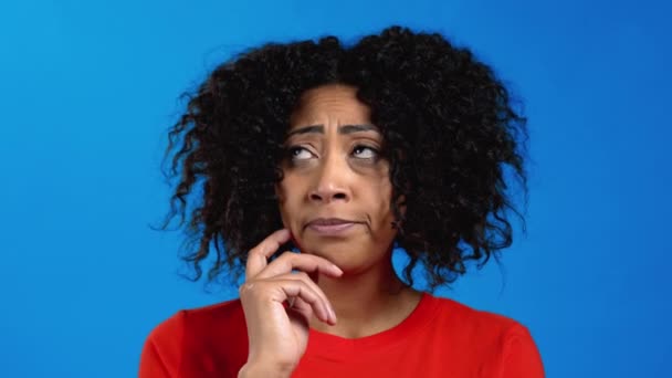 Tænker blandet race kvinde ser op og rundt på blå studie baggrund. Pensive ansigtsudtryk. Temmelig afro model med attraktivt udseende. – Stock-video