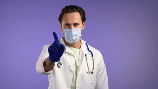 Retrato de un médico serio que muestra un gesto de rechazo por señal de stop finger. Oficial médico de bata blanca aislado sobre fondo violeta. — Vídeos de Stock