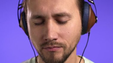 Yakışıklı genç adam müzikten hoşlanıyor. Stüdyoda kulaklıklarla gülüyor. Violet 'in arka planında. Yakın plan yüz. Dans, radyo konsepti.