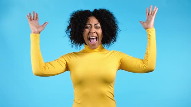 Woman is very glad, she screaming loud, sincere rejoices. Afro girl trying to get attention. Concept of sales, profitable offer. Excited happy lady on blue studio background. — Stock Video