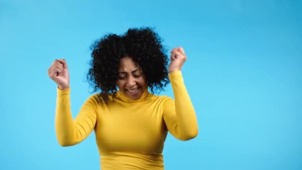 Μικτή γυναίκα φυλή με afro hairstyle χορεύουν θετικά σε μπλε φόντο στούντιο. Όμορφο γυναικείο μοντέλο με κίτρινη στολή. Κόμμα, ευτυχία, ελευθερία, έννοια της νεολαίας. — Αρχείο Βίντεο