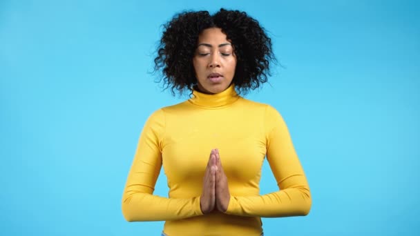 Femme africaine calme priant avec les mains ensemble symbolisant la prière et la gratitude. Mudra. Concept de yoga. Fond studio lumière bleue. — Video