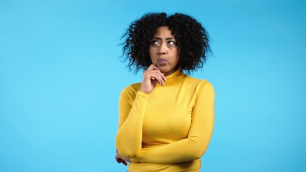 Pensando mulher de raça mista olhando para cima e ao redor no fundo do estúdio azul. Expressões faciais pensativas. Modelo afro bonita com aparência atraente — Vídeo de Stock