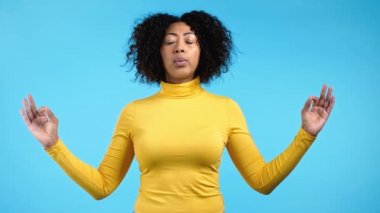 Sarılar içindeki sakin Afrikalı kadın dinleniyor, meditasyon yapıyor. Sakinleşiyor, derin derin derin nefes alıyor. Mavi stüdyo arka planında. Yoga konsepti.