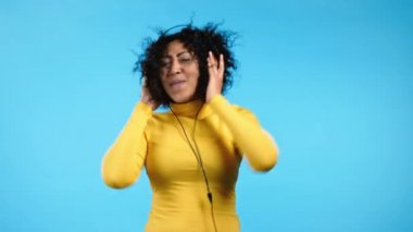 Mavi arka planda kulaklıkla dans eden Afrikalı Amerikalı kadın. Kız müzik yüzünden kafayı buluyor. Radyo, mutluluk, özgürlük, gençlik kavramı.