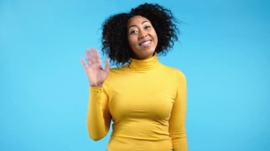 Afrikalı dost canlısı kadın el sallıyor. Merhaba. Selamlar, kameraya merhaba deyin. Mavi stüdyo geçmişinde güzel bir genç kız. 4k