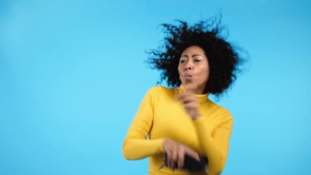 Mulher de raça mista ouvindo música por alto-falante portátil sem fio - sistema de som moderno. Senhora dançando, desfrutando no fundo do estúdio azul. Ela se move para o ritmo da música. — Vídeo de Stock