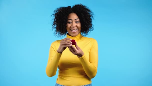 Kecewa african marah wanita, dia tidak seperti hadiah. Wanita cantik dengan pakaian kuning memegang kotak perhiasan kecil dengan lamaran pernikahan dengan latar belakang biru. — Stok Video