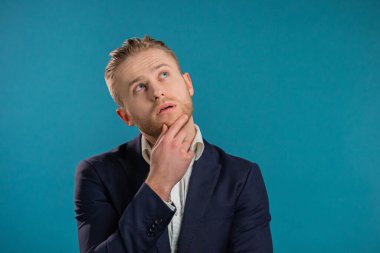 Düşünen bir iş adamı mavi arka plana bakıyor. Düşünceli yüz ifadeleri. Kampanya takımındaki yakışıklı adam..