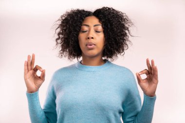 Mavi elbiseli sakin Afrikalı kadın dinleniyor, meditasyon yapıyor. Sakinleşir, beyaz stüdyo arka planında derin derin nefes alır. Yoga konsepti.