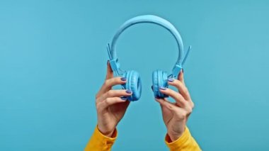 Mavi stüdyo arka planında kablosuz kulaklıklı bir kadının elleri. Müzik, radyo konsepti.