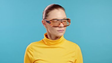 Mavi stüdyo arka planında neon gözlüklerle dans eden güzel bir kadın. Sarı elbiseli bir model. Parti, mutluluk, özgürlük, gençlik kavramı.