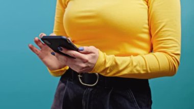 Mavi arka planda cep telefonu kullanan bir kadının elleri. Teknoloji, sosyal ağ, internet kavramı.