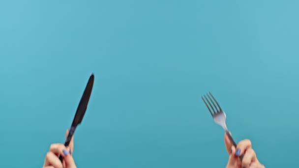 Çatal ve bıçaklı kadın elleri. Mavi stüdyo arka planında çatal bıçak takımı olan bir bayan yemek servisini bekliyor. Sadece eller.. — Stok video