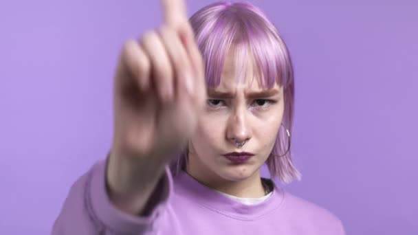 Портрет серьезной модной женщины, показывающей отвергающий жест указательным знаком. Девушка изолирована на фиолетовом фоне. — стоковое видео