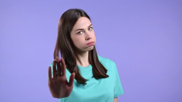 Portrait of serious woman showing rejecting gesture by stop palm hand sign. Girl isolated on violet background. — Stock Video