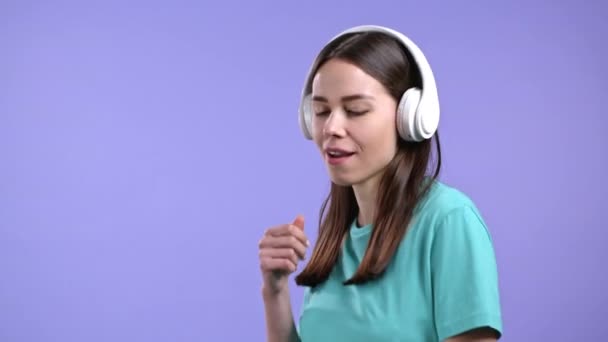 Mujer atractiva con auriculares blancos sobre fondo de estudio violeta. Retrato de chicas lindas. Música, radio, felicidad, libertad, concepto de juventud. — Vídeos de Stock